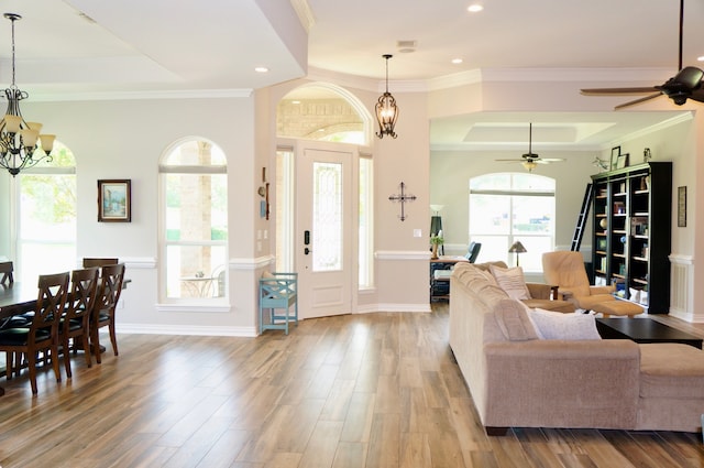 interior space with a raised ceiling, ornamental molding, ceiling fan with notable chandelier, and light wood-type flooring