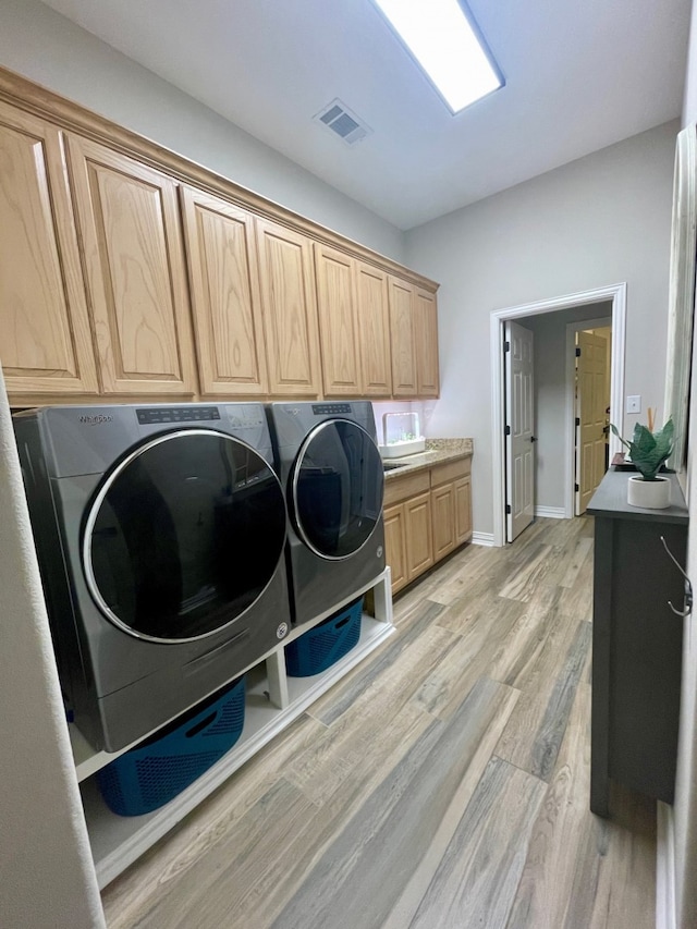 clothes washing area with cabinets, washing machine and dryer, and light hardwood / wood-style floors