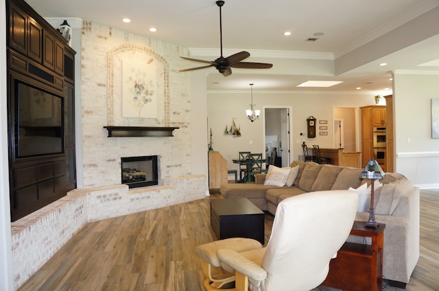 living room featuring a fireplace, wood-type flooring, ornamental molding, and ceiling fan with notable chandelier