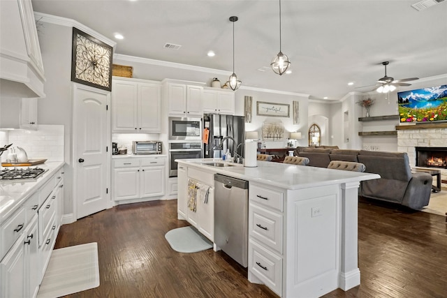 kitchen featuring stainless steel appliances, ceiling fan, crown molding, white cabinetry, and an island with sink