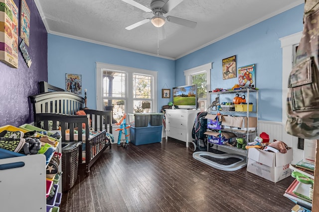 bedroom with ceiling fan, dark wood-type flooring, a textured ceiling, a nursery area, and ornamental molding