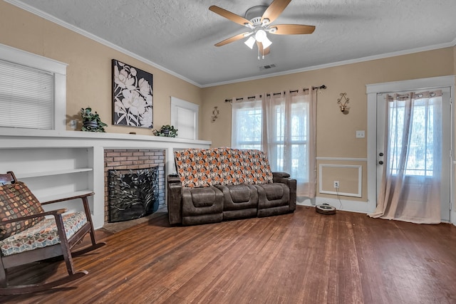 living room featuring ceiling fan, a brick fireplace, dark hardwood / wood-style flooring, a textured ceiling, and ornamental molding