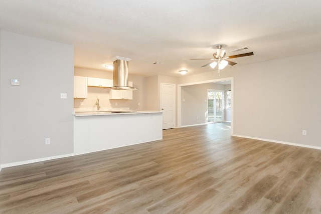 unfurnished living room with visible vents, light wood-style floors, a ceiling fan, a sink, and baseboards