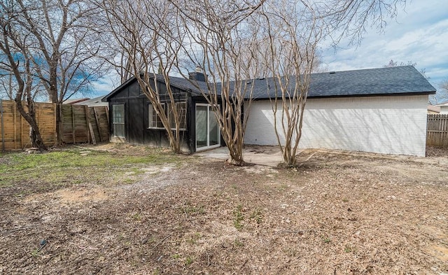 rear view of property with a shingled roof, a fenced backyard, and brick siding