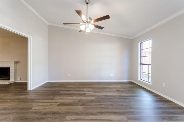 empty room featuring dark wood-style floors, a brick fireplace, crown molding, and baseboards