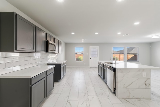 kitchen featuring appliances with stainless steel finishes, decorative backsplash, a center island with sink, and sink