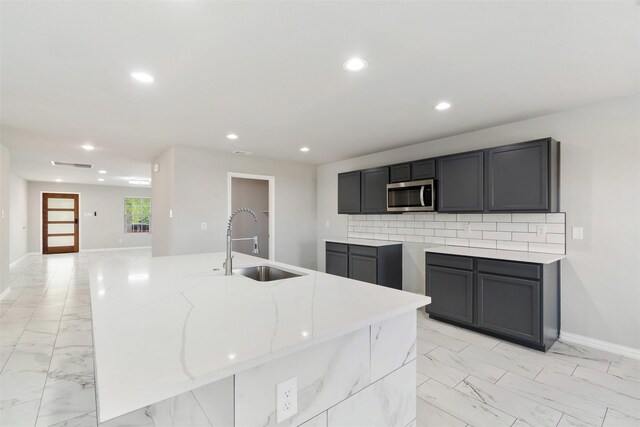 kitchen featuring a kitchen island with sink, light stone counters, tasteful backsplash, and sink