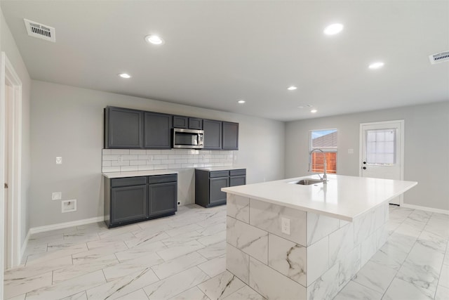 kitchen featuring sink, an island with sink, gray cabinetry, and decorative backsplash