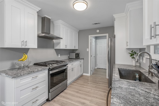 kitchen with white cabinetry, sink, wall chimney range hood, appliances with stainless steel finishes, and light wood-type flooring