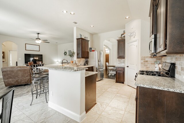 kitchen featuring backsplash, ceiling fan, appliances with stainless steel finishes, light stone counters, and a breakfast bar area