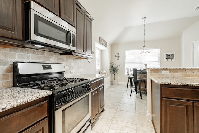 kitchen featuring dark brown cabinets, light stone countertops, stainless steel appliances, and vaulted ceiling