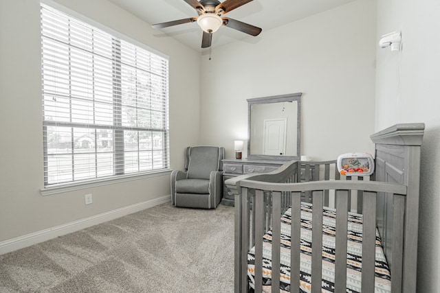 carpeted bedroom featuring multiple windows, ceiling fan, and a nursery area