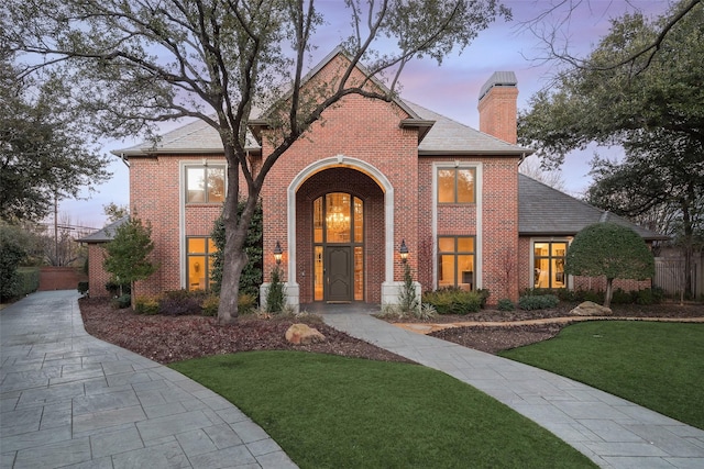 view of front of property with brick siding, a lawn, and a chimney