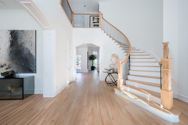 foyer with crown molding, a towering ceiling, and light hardwood / wood-style flooring