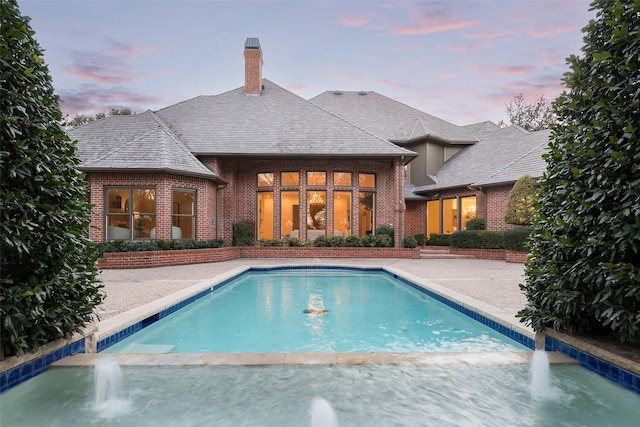 pool at dusk featuring pool water feature