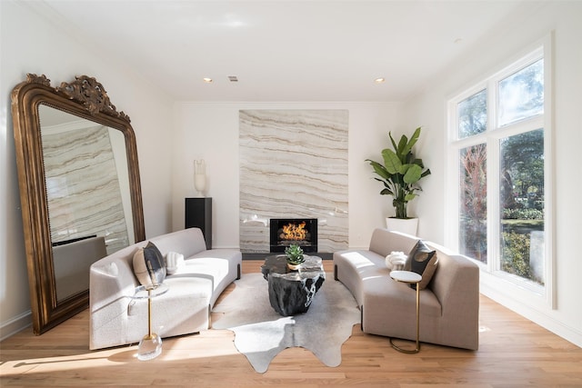 living room with a high end fireplace, ornamental molding, a healthy amount of sunlight, and light wood-type flooring