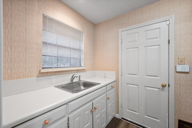 5400 Emerald Park Blvd, Arlington, TX 76017 - kitchen featuring wallpapered walls, a sink, light countertops, a textured ceiling, and white cabinetry