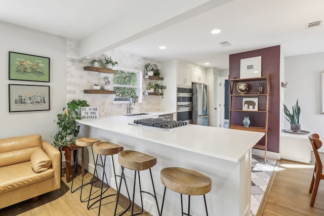 kitchen featuring stainless steel appliances, kitchen peninsula, a breakfast bar, white cabinets, and light wood-type flooring