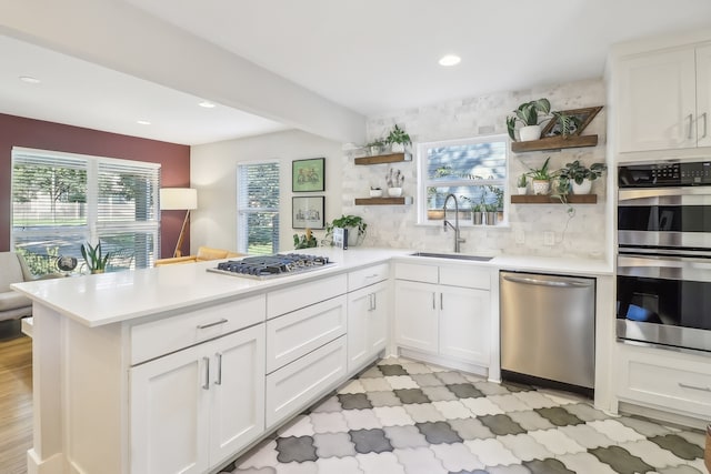 kitchen with sink, backsplash, kitchen peninsula, white cabinets, and appliances with stainless steel finishes