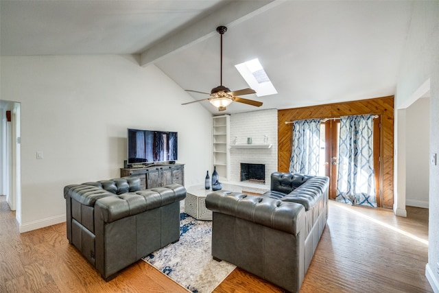 living room with lofted ceiling with skylight, wooden walls, ceiling fan, light wood-type flooring, and a fireplace