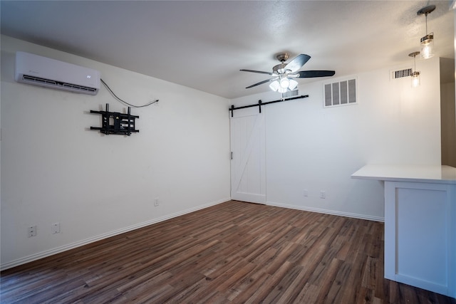 unfurnished room featuring ceiling fan, a barn door, dark hardwood / wood-style flooring, and a wall mounted AC