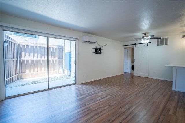 unfurnished living room with a textured ceiling, a barn door, dark hardwood / wood-style flooring, and a wall mounted air conditioner