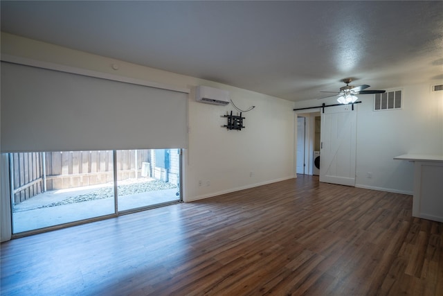 unfurnished living room with dark hardwood / wood-style flooring, a barn door, a wall unit AC, and ceiling fan