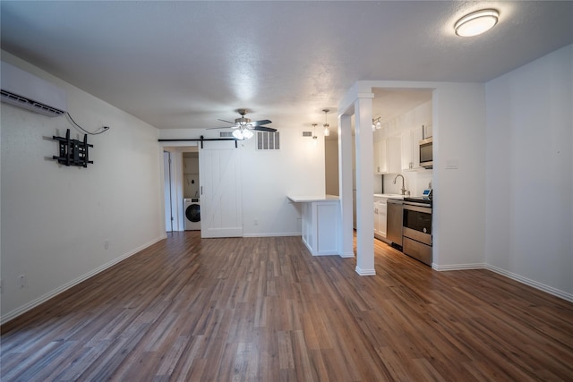 unfurnished living room featuring a wall mounted AC, dark wood-type flooring, sink, a barn door, and washer / clothes dryer