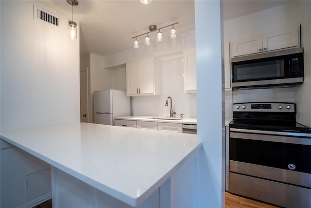 kitchen with white cabinetry, sink, hanging light fixtures, light hardwood / wood-style floors, and appliances with stainless steel finishes