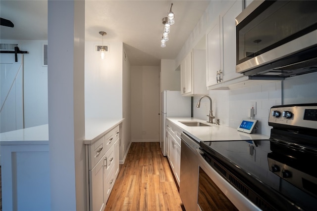 kitchen featuring pendant lighting, white cabinets, a barn door, light wood-type flooring, and stainless steel appliances