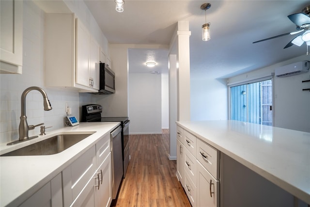 kitchen featuring stainless steel appliances, a wall unit AC, light hardwood / wood-style flooring, white cabinets, and hanging light fixtures