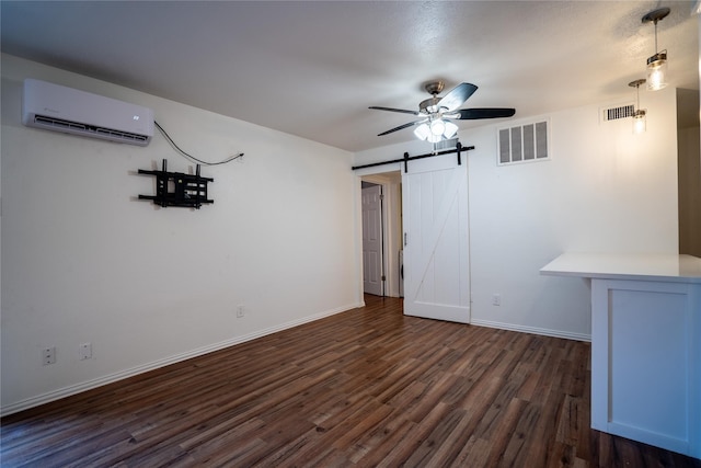 interior space with dark hardwood / wood-style flooring, a barn door, a wall unit AC, and ceiling fan