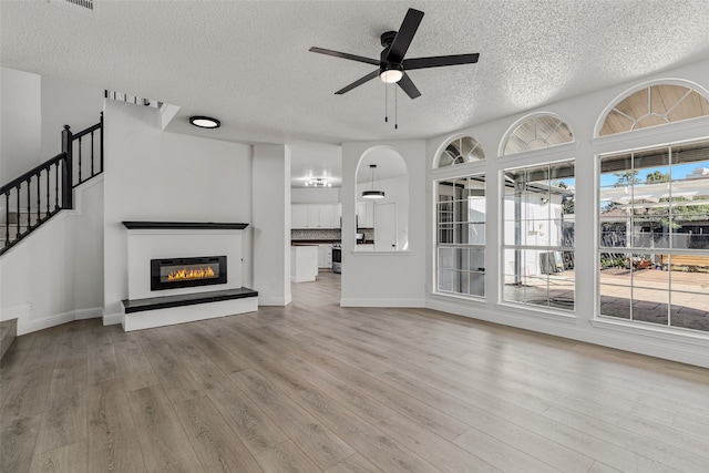 unfurnished living room with ceiling fan, a textured ceiling, and light wood-type flooring