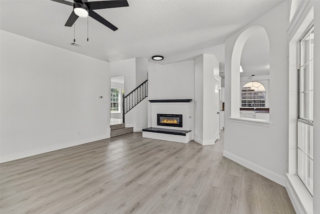 unfurnished living room with a textured ceiling, light hardwood / wood-style flooring, and ceiling fan