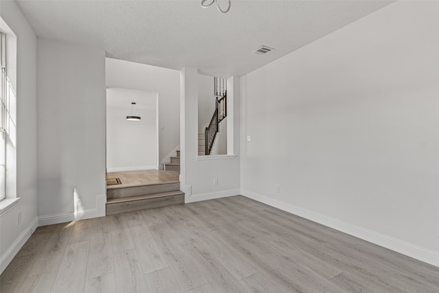 empty room with light wood-type flooring, a textured ceiling, and a wealth of natural light