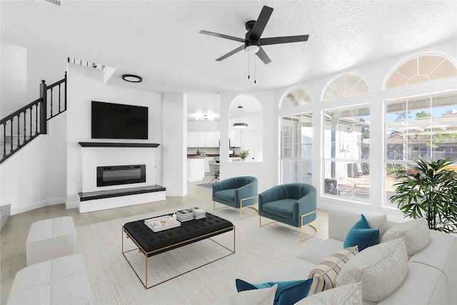 living room featuring ceiling fan, light wood-type flooring, and a textured ceiling