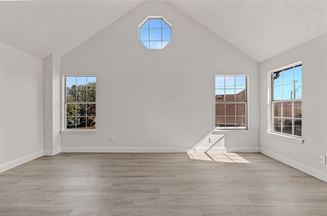 unfurnished room featuring light hardwood / wood-style floors, a textured ceiling, and high vaulted ceiling