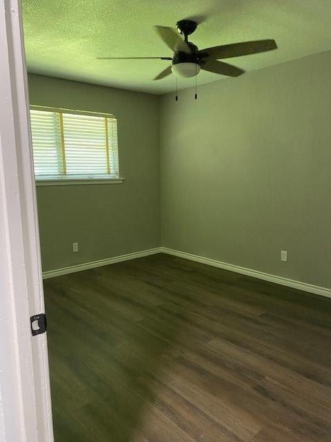 spare room with a textured ceiling, dark wood-style flooring, and baseboards