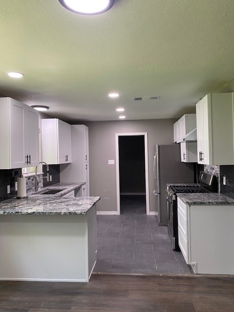 kitchen featuring stainless steel range with gas cooktop, dark hardwood / wood-style floors, kitchen peninsula, decorative backsplash, and white cabinets