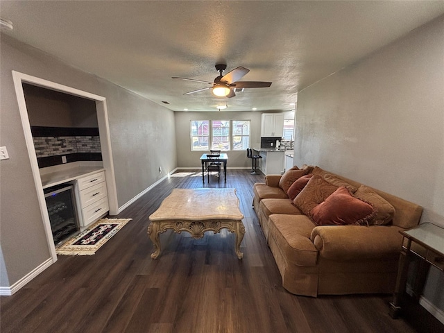 living room featuring dark wood-style floors, wine cooler, a fireplace, a ceiling fan, and baseboards