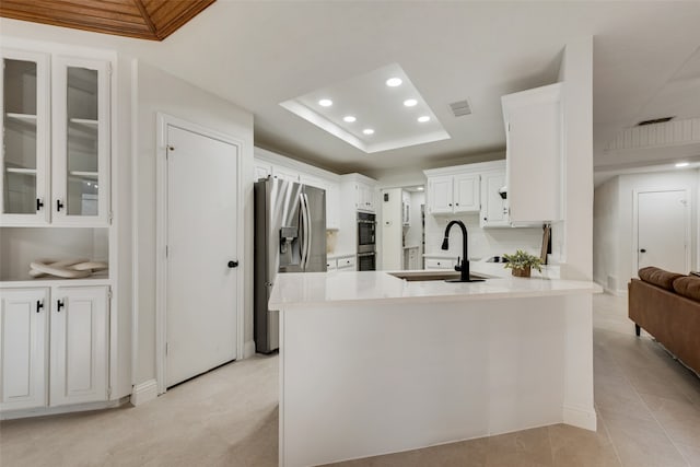 kitchen featuring white cabinetry, sink, stainless steel appliances, a raised ceiling, and kitchen peninsula