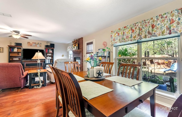 dining space with ceiling fan, wood-type flooring, and a brick fireplace