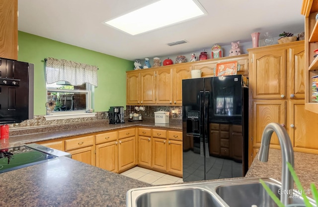 kitchen featuring light tile patterned floors, tasteful backsplash, black fridge, and sink