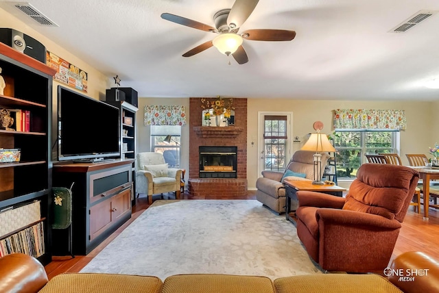 living room with ceiling fan, light wood-type flooring, and a brick fireplace