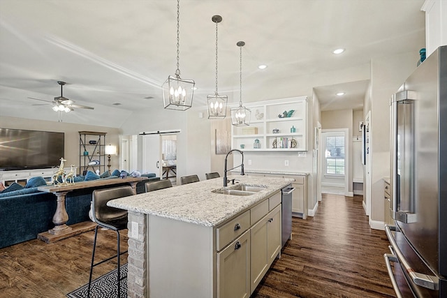 kitchen with light stone counters, stainless steel appliances, a barn door, a center island with sink, and lofted ceiling