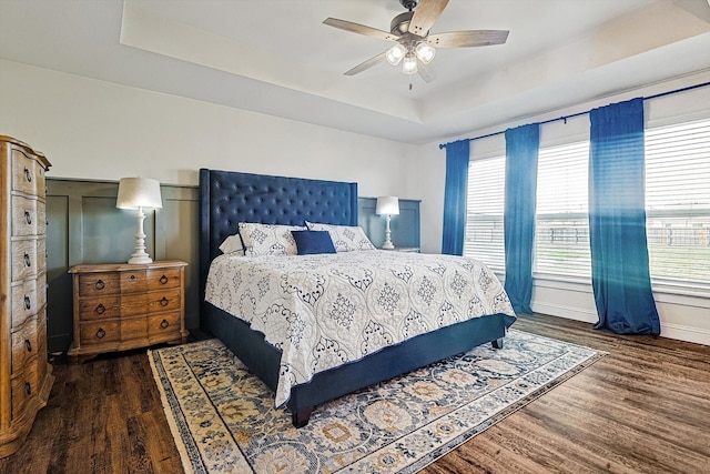 bedroom with ceiling fan, dark hardwood / wood-style floors, and a tray ceiling