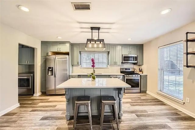 kitchen featuring appliances with stainless steel finishes, washer / clothes dryer, light hardwood / wood-style flooring, and hanging light fixtures