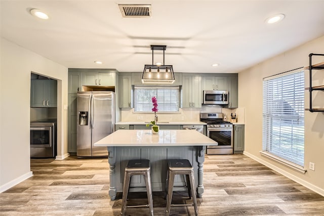 kitchen featuring stainless steel appliances, sink, decorative light fixtures, light hardwood / wood-style flooring, and a center island