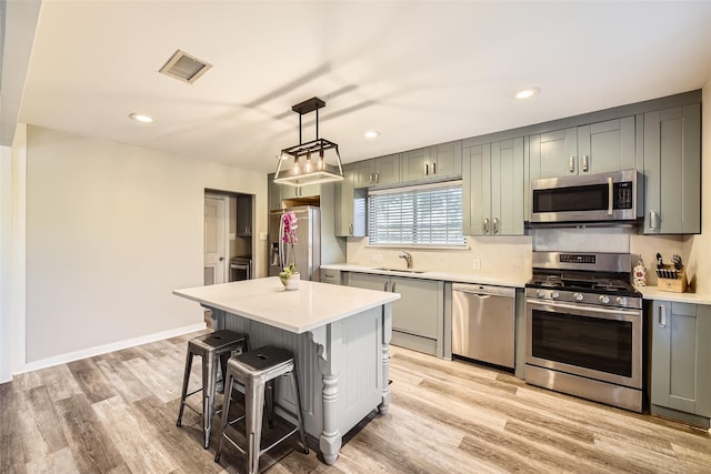 kitchen featuring sink, light hardwood / wood-style floors, appliances with stainless steel finishes, decorative light fixtures, and a kitchen island