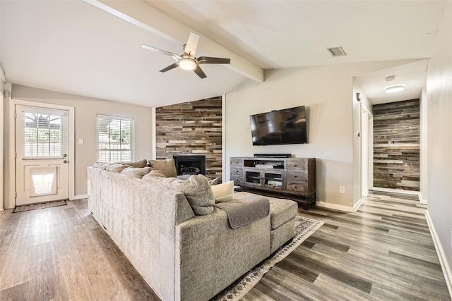 living room with ceiling fan, vaulted ceiling with beams, wood walls, wood-type flooring, and a fireplace